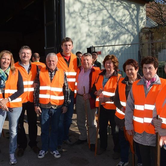 Eine Gruppe von Menschen in orangefarbenen Sicherheitswesten steht zusammen vor einem Gebäude. Sie lächeln und scheinen für ein Foto zu posieren.