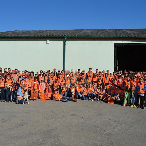 Eine große Gruppe von Menschen in orangefarbenen Westen und mit Stöcken posiert für ein Foto vor einem Gebäude.