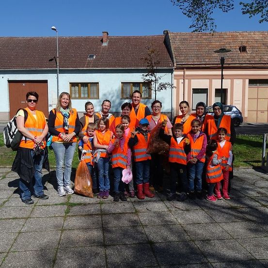 Eine Gruppe von Erwachsenen und Kindern in orangefarbenen Westen posiert für ein Foto vor einem Gebäude.