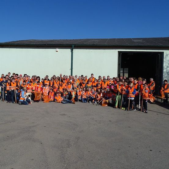 Eine Gruppe von Menschen in orangefarbenen Westen, die Besen und Taschen halten, posiert für ein Foto vor einem Gebäude.