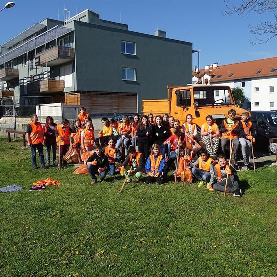 Eine Gruppe von Menschen in orangefarbenen Westen posiert für ein Foto vor einem Gebäude mit einem gelben Lastwagen im Hintergrund.