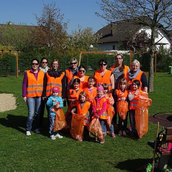 Eine Gruppe von Erwachsenen und Kindern in orangefarbenen Westen und mit orangefarbenen Tüten posiert für ein Foto im Park.