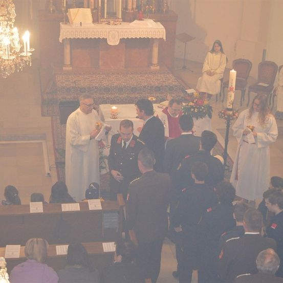 Eine religiöse Zeremonie findet in einer Kirche statt, an der ein Priester und Militäroffiziere teilnehmen. Der Altar ist mit Kerzen und Blumen geschmückt.