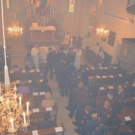 Eine Kirchenmesse mit Teilnehmern auf den Bänken, einem Priester am Altar und einer Gruppe uniformierter Personen im Vordergrund.