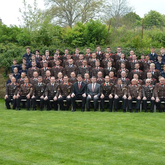 Eine Gruppe von Militäroffizieren und Beamten in Uniform posiert für ein Foto auf einer Wiese.
