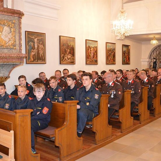 Eine Gruppe uniformierter Personen, möglicherweise eine Militär- oder Polizeiakademie, sitzt auf einer Kirchenbank. Sie tragen Medaillen und scheinen einer Predigt zuzuhören.