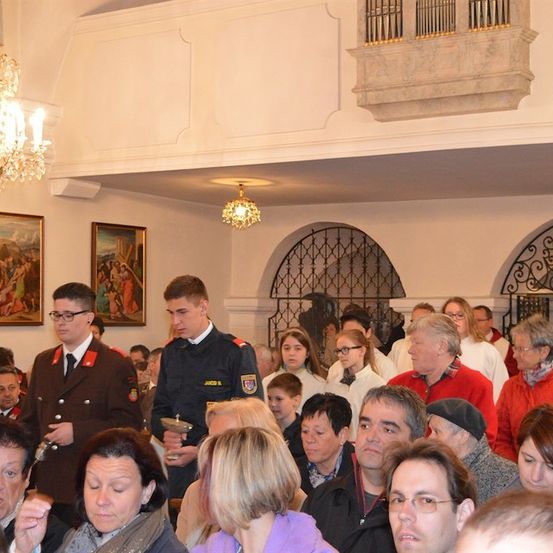 Eine feierliche Versammlung in einer Kirche mit zwei uniformierten Männern, einer hält einen Kelch, und eine Menge Menschen hört aufmerksam zu.