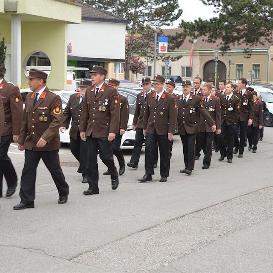 Eine Gruppe uniformierter Personen, möglicherweise Militär oder Polizei, marschiert bei einer Parade auf einer Straße.