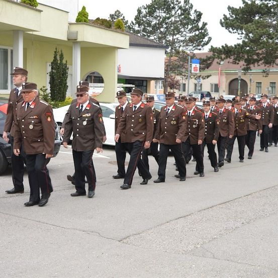 Eine Gruppe uniformierter Personen, möglicherweise Militär oder Polizei, marschiert bei einer Parade auf einer Straße.