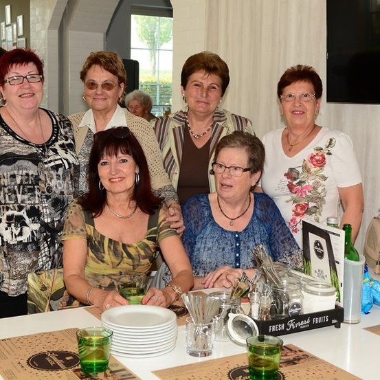 Eine Gruppe von Frauen lächelt und posiert für ein Foto an einem Tisch mit Tellern, Gläsern und einer Vase mit Blumen.