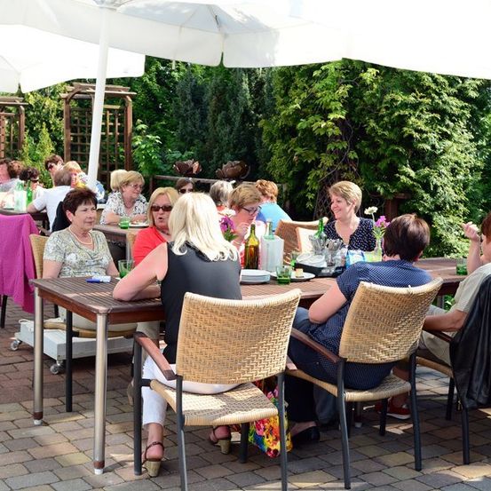 Eine Gruppe älterer Frauen sitzt an einem Tisch in einem Outdoor-Restaurant und genießt ihr Essen unter einem weißen Schirm.