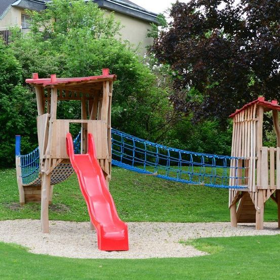 Eine Holzspielanlage mit einer roten Rutsche und einer blauen Seilleiter auf einer Rasenfläche.