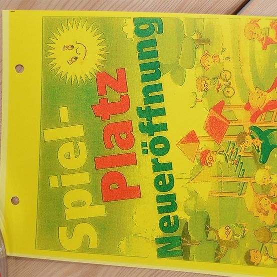 Ein gelbes Poster mit einer Karikatur von Kindern, die auf einem Spielplatz spielen. Der Titel 'Spielplatz Neueroffnung' ist in roten und grünen Buchstaben geschrieben. Die Sonne scheint hell im Hintergrund.