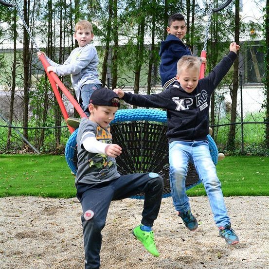 Vier Jungen spielen auf einer Schaukel in einem Park. Ein Junge springt von der Schaukel, während ein anderer Junge die Schaukel festhält.