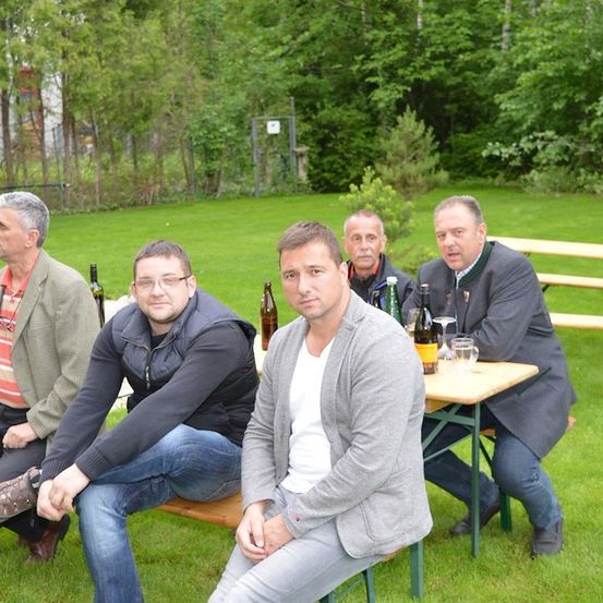Fünf Männer sitzen auf Bänken in einem Park, einige mit Weinglas, andere mit Flaschen. Sie scheinen in ein Gespräch vertieft zu sein.