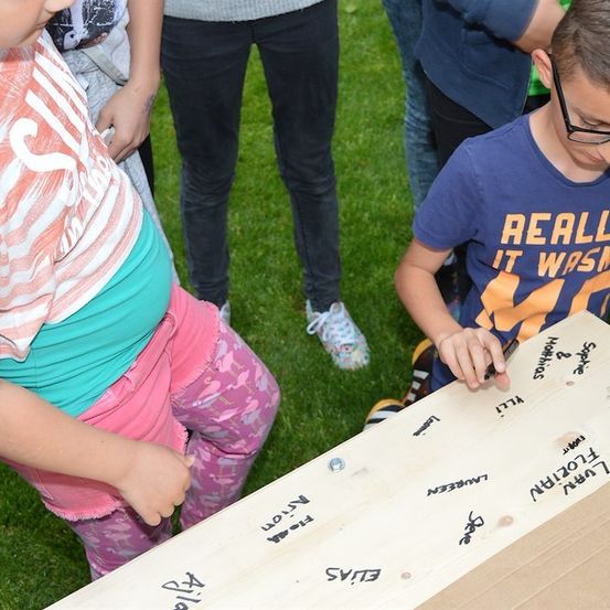 Eine Gruppe von Kindern spielt ein Spiel auf einem Holzbrett mit Schrift darauf.