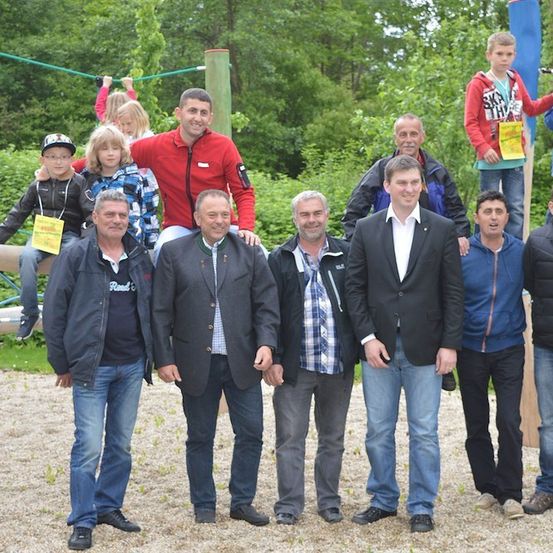 Eine Gruppe von Männern und Kindern posiert für ein Foto in einem Park mit einem Spielplatz im Hintergrund.