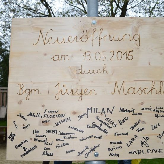 Ein Holzschild mit handgeschriebenem Text auf Deutsch, 'Neueröffnung am 13.05.2015 durch Bgm. Jürgen Maschl'. Darunter sind zahlreiche Namen in kursiver Schrift geschrieben.