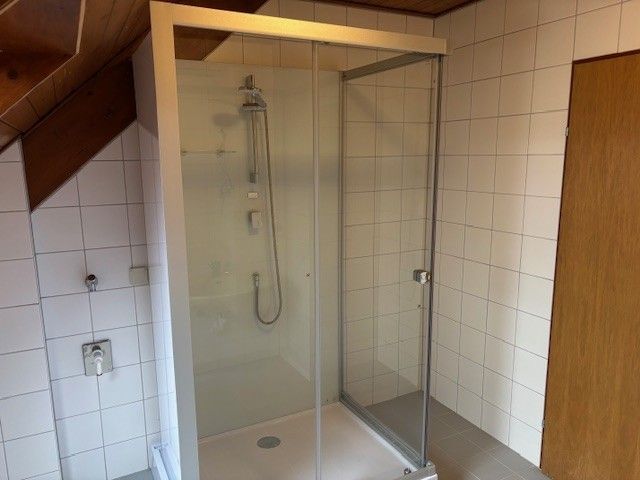 Ein Bild eines Badezimmers mit gefliesten Wänden und einer Glasdusche. Es gibt einen Duschkopf und einen Wasserhahn an der Wand montiert.