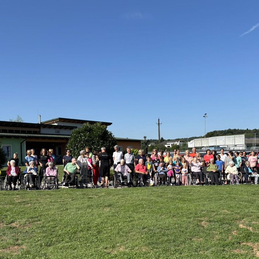 Eine Gruppe von Menschen, darunter viele in Rollstühlen, posiert für ein Foto an einem sonnigen Tag auf einer Rasenfläche.