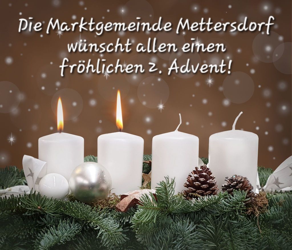 Ein Kranz aus Tannenzweigen umgibt vier weiße Kerzen, von denen drei brennen. Eine Botschaft in weißer Schrift lautet 'Die Marktgemeinde Mettersdorf wünscht allen einen frohlichen 2. Advent!' mit Schneeflocken im Hintergrund.