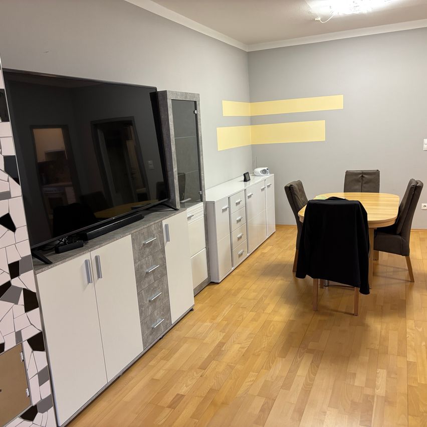 Ein modernes Innendesign mit einem großen Flachbildfernseher, Holzboden und einem runden Esstisch mit Stühlen.