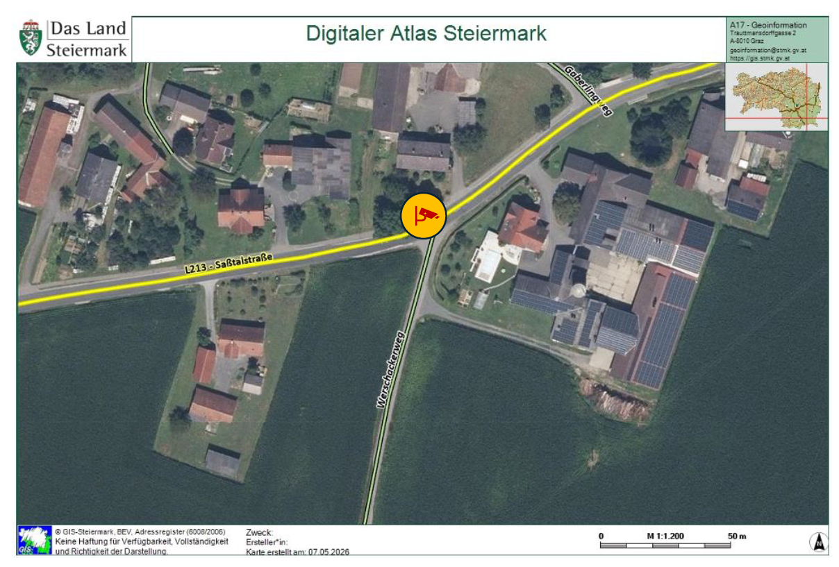 An aerial image of a rural area, showing houses, a road, and a yellow path. The image has a map scale and date stamp.