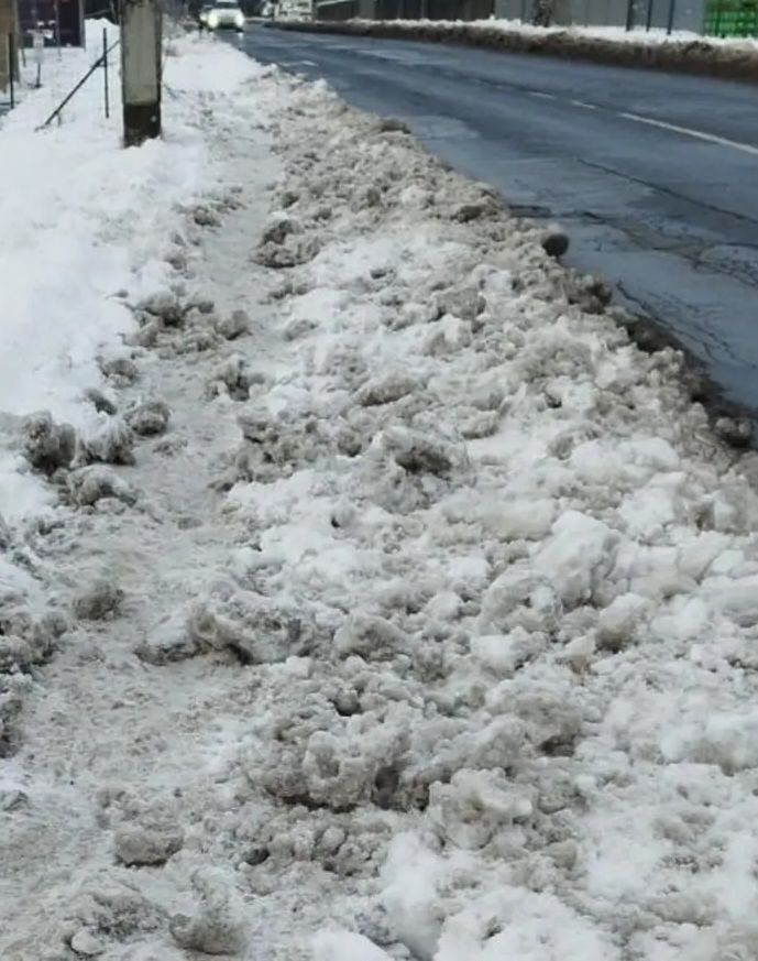 A road with snow pushed to the side and a sidewalk with melted snow.