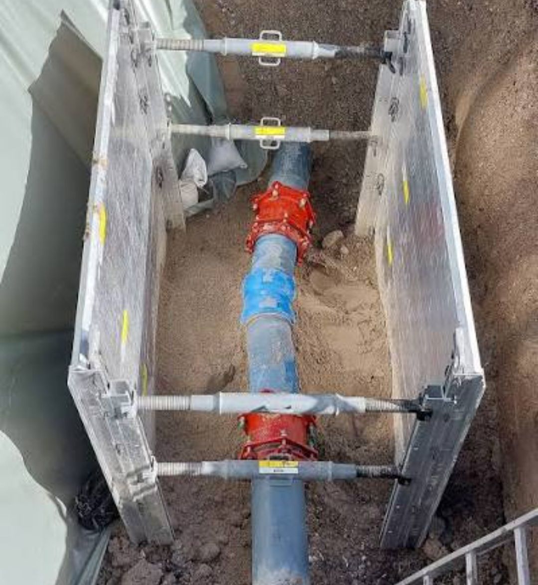 Eine große Rohrleitung, die durch Metallstreben gesichert ist, ist unterirdisch vergraben. Das Rohr hat ein blaues und rotes Ventil.