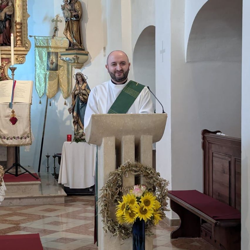 Ein Priester steht an einer Kanzel in einer Kirche, umgeben von religiösen Symbolen und Blumen.