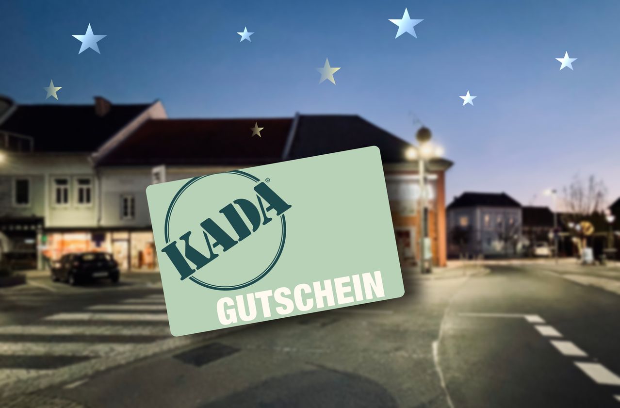 Eine grüne Karte mit dem Wort 'KADA' und dem Text 'GUTSCHEIN' vor einem unscharfen Hintergrund mit Gebäuden und Sternen.