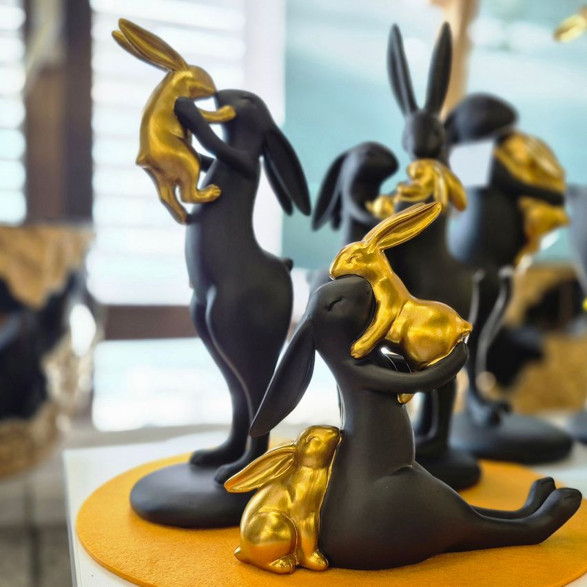 A set of black and gold rabbit figurines on a yellow circular base, with one rabbit holding a smaller golden rabbit.