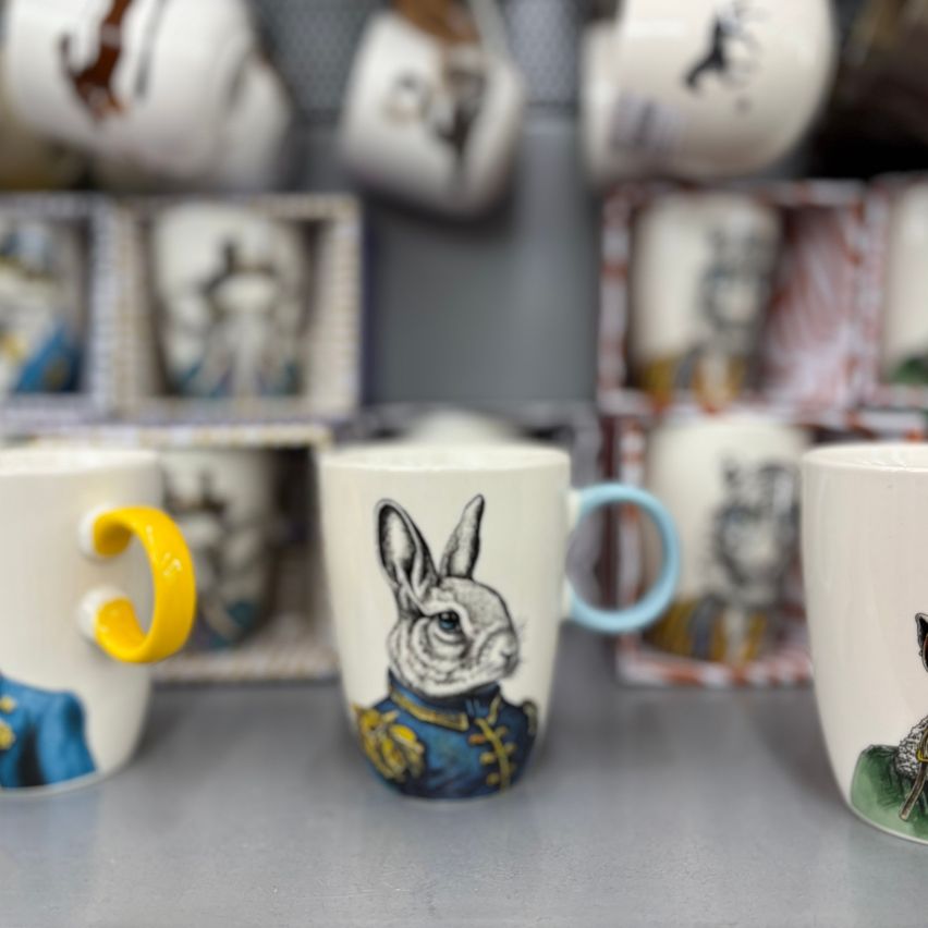 Three ceramic mugs with rabbit, cat, and deer designs on a shelf, with a yellow-handled mug in the foreground.
