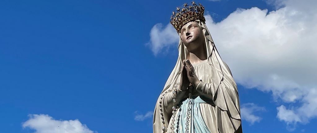 Eine Statue einer Frau, möglicherweise die Jungfrau Maria, ist in einer betender Haltung mit einer Krone auf dem Kopf dargestellt.