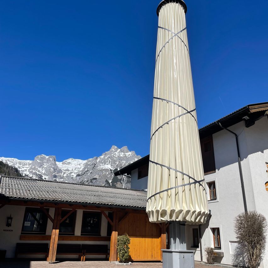 A tall, cylindrical structure stands in front of a building with a snowy mountain range in the background.