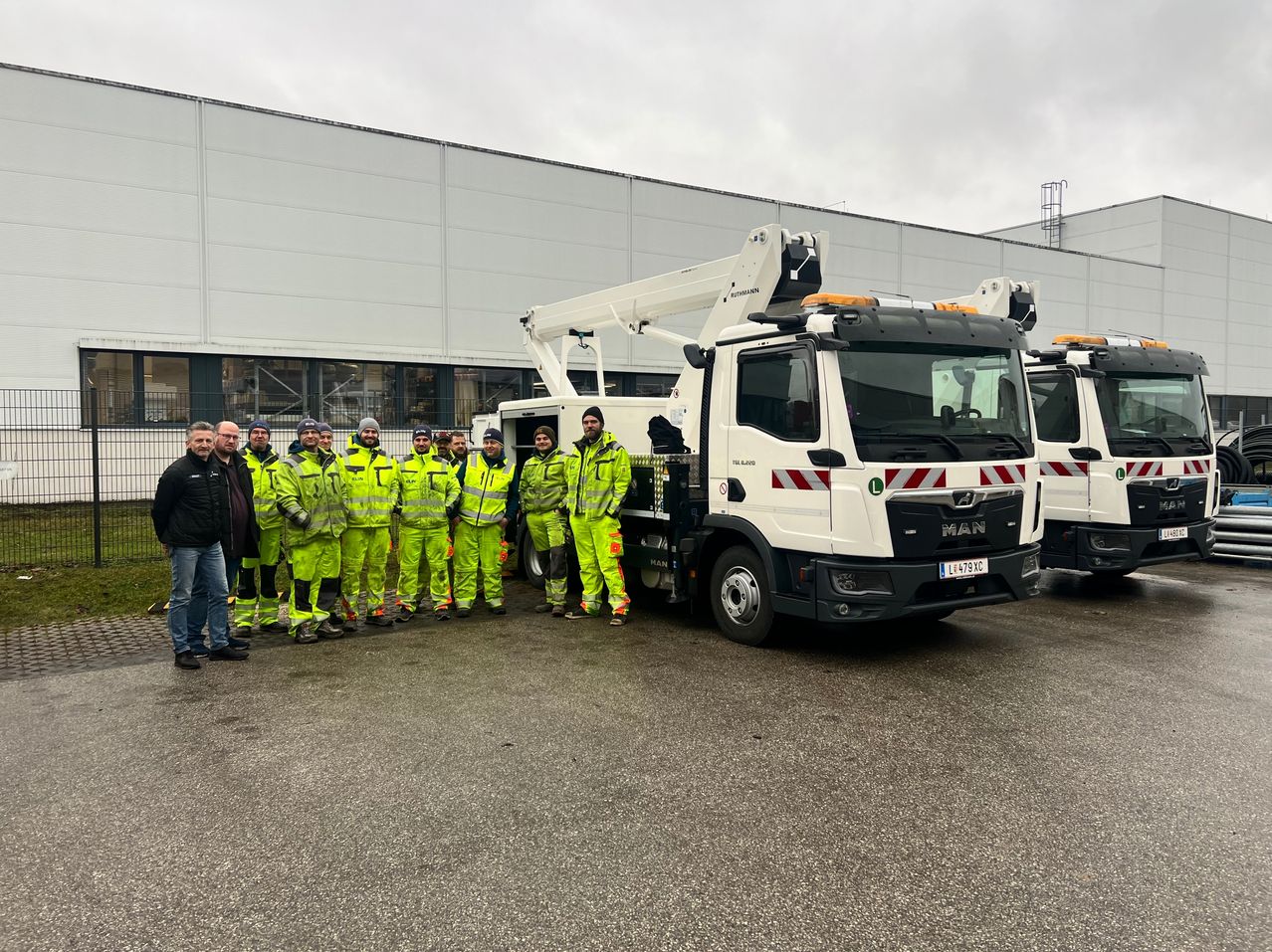 Eine Gruppe von Arbeitern in reflektierenden Warnwesten posiert vor zwei Trucks.