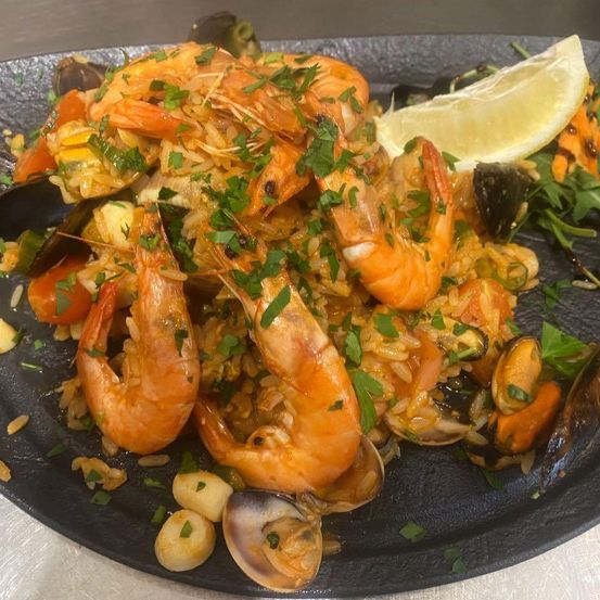 A plate of seafood paella, topped with shrimp, mussels, and a slice of lemon, garnished with parsley.
