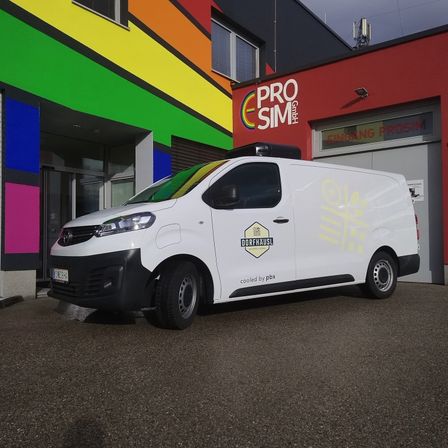 Ein weißer Lieferwagen steht vor einem farbenfrohen Gebäude mit einem Schild, das 'Pro Sim' besagt.