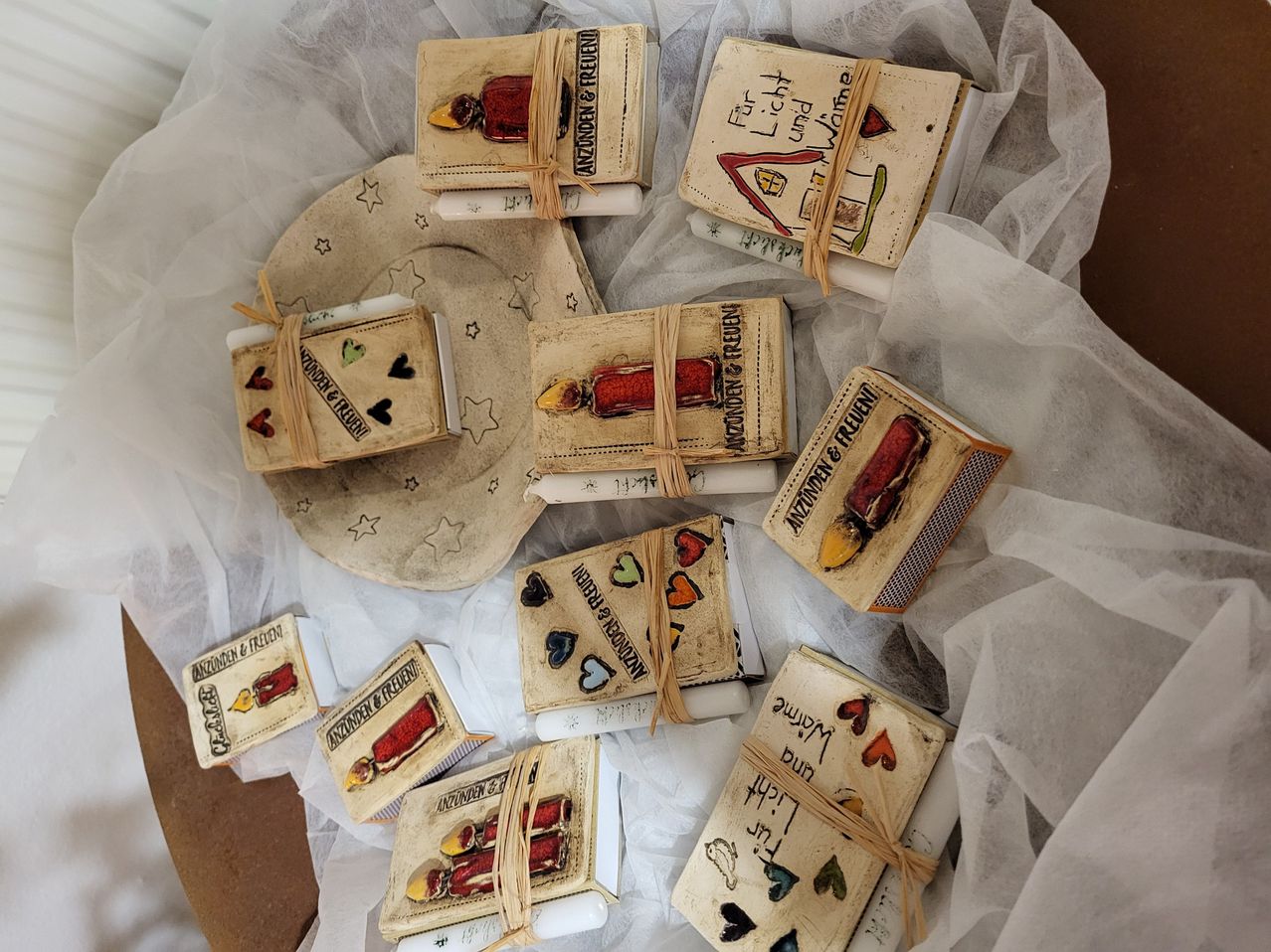 Eine Sammlung von Miniaturbüchern mit dekorativen Einbänden und Bindfäden, die Illustrationen von Herzen, Sternen und verschiedenen Motiven zeigen, auf einem weißen Tuch präsentiert.