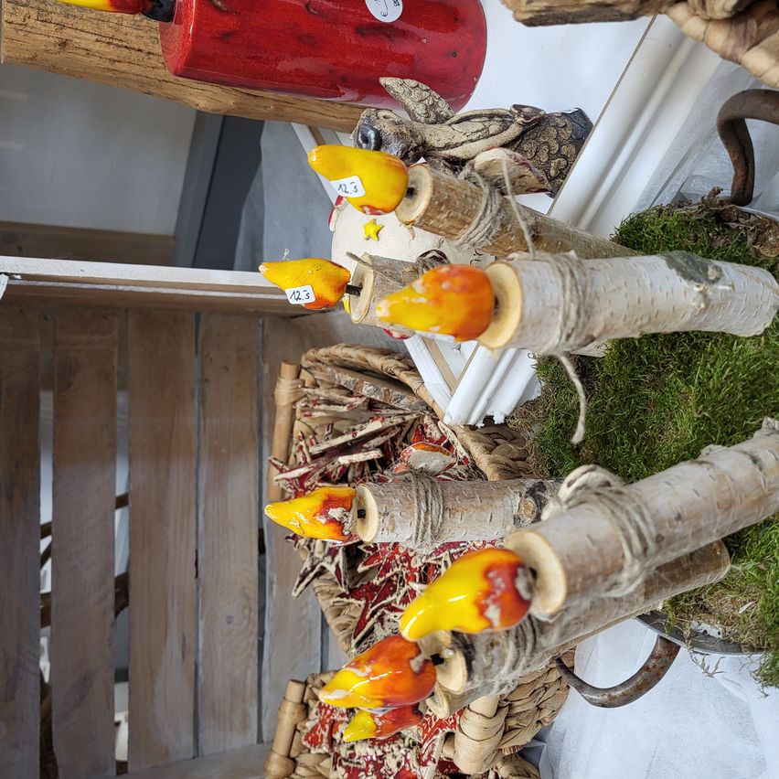 Eine Sammlung dekorativer Kerzen aus Birkenrinde. Jede Kerze hat eine gelbe und orange Flamme und ist rustikal verpackt. Ausgestellt auf einer moosigen Oberfläche mit anderen Dekorationsartikeln.