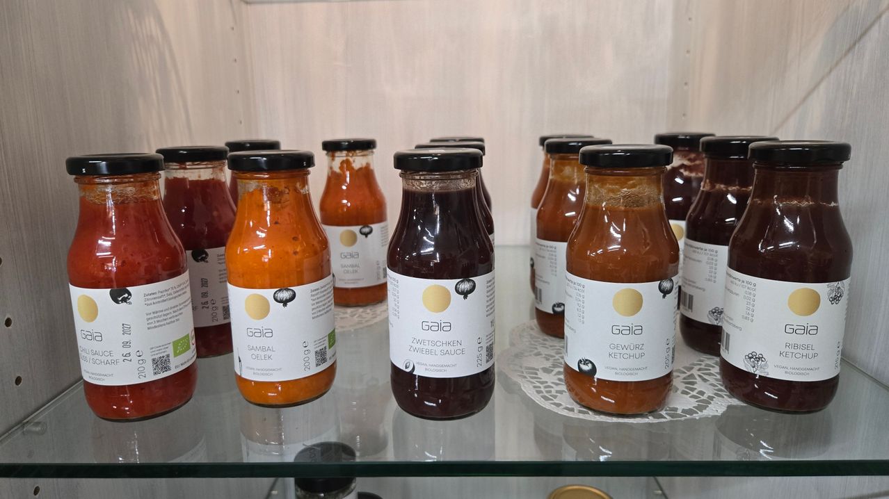 Eine Ausstellung verschiedener Saucenflaschen, einschließlich Sambal Oelek, Zwiebelsauce und Gewürzketchup, alle mit dem Markennamen Gaia gekennzeichnet.