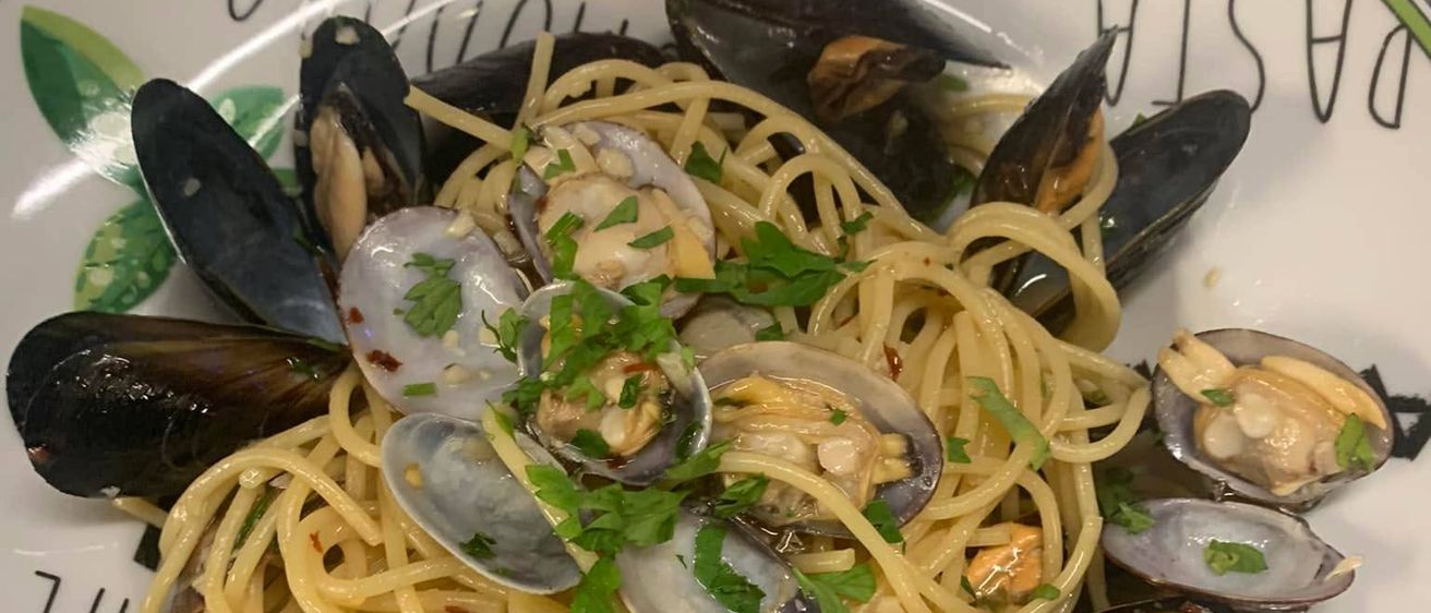 Ein Teller mit Spaghetti und Muscheln, garniert mit Petersilie, auf einem Teller mit grünem Rand und einer Tomate obenauf.
