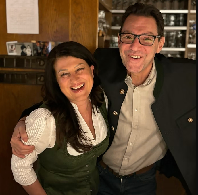 Ein Mann und eine Frau lächeln und posieren für ein Foto in einem Raum mit Holzwänden und Regalen mit Gläsern.