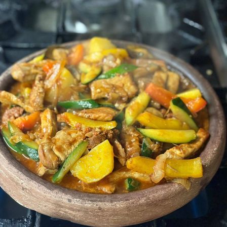 Ein hölzerner Teller gefüllt mit einem bunten Wok-Gemüse mit Fleisch, Zucchini und Karotten, auf einem Herd platziert.