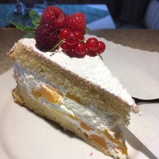 Ein Stück Kuchen mit cremiger Füllung, bestreut mit weißem Pulver, Himbeeren und roten Johannisbeeren auf einem weißen Teller.