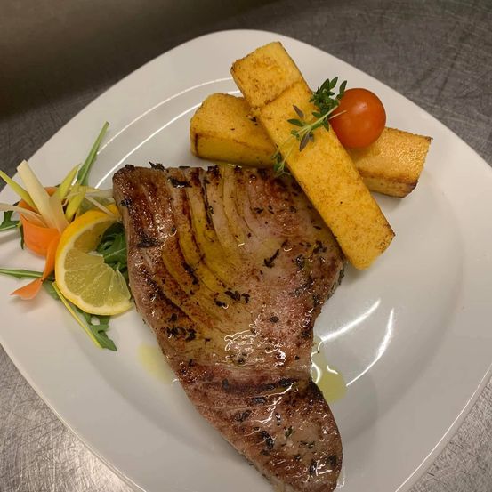 Ein weißer Teller mit gegrilltem Steak, Zitronenscheiben und gerösteten Brotstücken.
