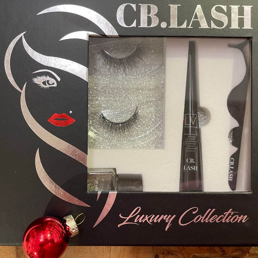 Eine schwarze Schachtel mit dem Text 'CB.LASH' zeigt im Ausschnitt Wimpern, eine Mascara-Bürste und eine rote Kugel. Im Inneren sind ein silbernes, glitzerndes Wimpernbild, eine Mascara-Flasche und eine Pinzette zu sehen. Darunter steht 'Luxury Collection' in Pink geschrieben.