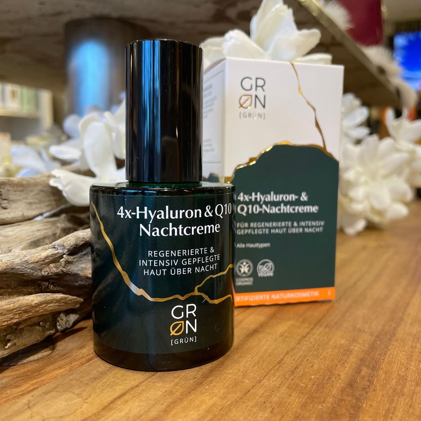 A bottle of 4x-Hyaluron & Q10 Nachtcreme is on a wooden table with a box. The product is vegan, certified organic, and intended for regeneration and intensive care.