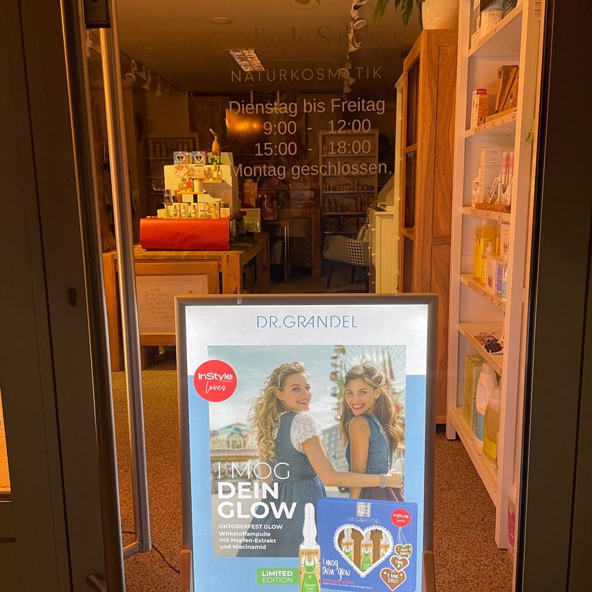 Ein Ladendisplay mit einem Schild, das die Öffnungszeiten anzeigt, und eine Produktwerbung mit zwei lächelnden Frauen.