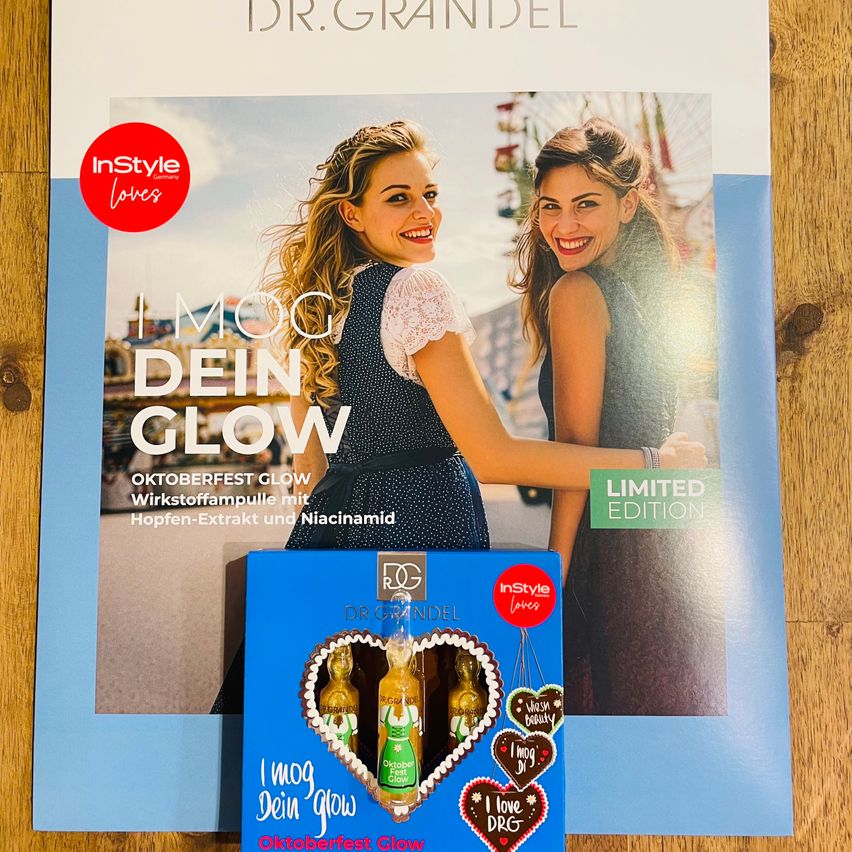Ein Zeitschriftencover mit zwei lächelnden Frauen, eine in einem gepunkteten Kleid und die andere in einem schwarzen Kleid, mit einer Produktbox im Vordergrund. Der Titel lautet 'I Mog Dein Glow' und 'Oktoberfest Glow'.